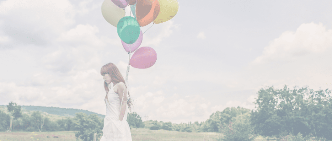 Frau läuft draußen mit bunten Luftballons an der Hand